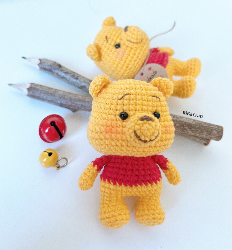 Pu&ograve; includere: Due orsi Winnie the Pooh all'uncinetto, uno con una camicia rossa e l'altro con un'etichetta marrone che dice "fatto a mano".