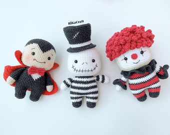 May include: Three crocheted Halloween characters: a vampire, a skeleton wearing a top hat, and a clown. The vampire is wearing a red cape and a black bow tie. The skeleton is wearing a black and white striped shirt. The clown is wearing a red and white striped shirt and a red wig.