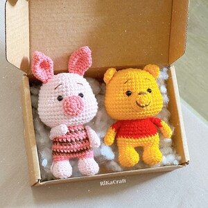 Pu&ograve; includere: Due giocattoli di peluche all'uncinetto in una scatola di cartone. Il primo giocattolo &egrave; un maiale rosa con strisce marroni e rosa. Il secondo giocattolo &egrave; un orso giallo con una camicia rossa.
