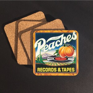 May include: A set of four square cork coasters. One coaster features a vintage-style design with the word "Peaches" in white script, a peach illustration, and the text "Records & Tapes."