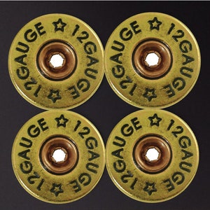 May include: Four gold-colored 12 gauge shotgun shell casings with black lettering. The casings are arranged in a square pattern.