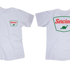 May include: White t-shirt with a red and green Sinclair logo featuring a dinosaur on the back and a smaller version of the logo on the front left chest.