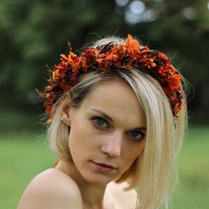 Può includere: Una donna con i capelli biondi indossa un vestito marrone senza spalle e una corona di fiori fatta di fiori secchi arancioni.
