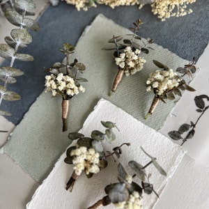May include: Four small bouquets of dried white flowers and eucalyptus leaves tied with twine, arranged on white and green paper.