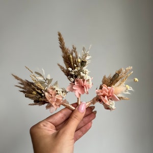 May include: Three small bouquets of dried flowers, each with pink flowers, white flowers, and dried grasses. The bouquets are tied together with a ribbon.