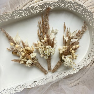 May include: Three small bouquets of dried flowers, tied with twine, in a white tray with a decorative lace edge.