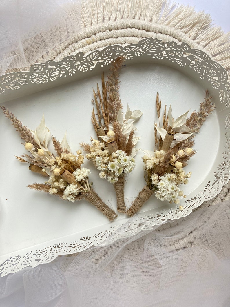 May include: Three small bouquets of dried flowers, tied with twine, in a white tray with a decorative lace edge.