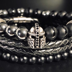 May include: A set of three black beaded bracelets with silver accents. The center bracelet features a silver helmet charm with black stones.