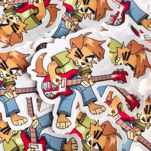 May include: A collection of stickers featuring a cartoon dog playing a red electric guitar. The dog is wearing a green shirt and blue jeans. The stickers have a white border and are scattered across a white surface.