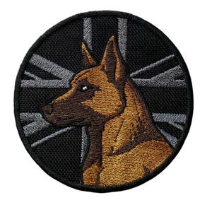 May include: Circular embroidered patch with a brown dog's head in profile, set against a black background with a gray Union Jack design. The patch has a black border.