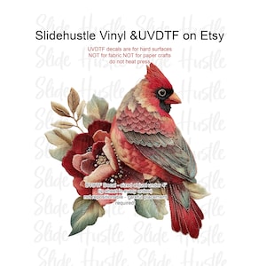 May include: A detailed UVDTF decal featuring a vibrant red cardinal perched on burgundy flowers with green and tan leaves. The text "Slidehustle Vinyl & UVDTF on Etsy" is at the top. The decal is sized under 4 inches.