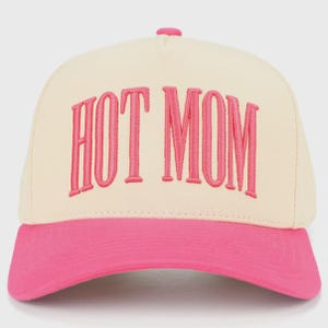 Puede incluir: Gorra de béisbol con corona color crema y visera rosa. La frase "HOT MOM" está bordada en rosa en la parte delantera de la gorra. La gorra tiene una visera curva y un botón en la parte superior.