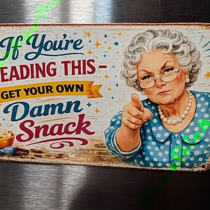 May include: A vintage-style metal sign with a humorous message. The sign features an illustration of an elderly woman pointing, with text that reads "If You're Reading This - Get Your Own Damn Snack." The sign has a distressed, aged appearance.