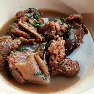 May include: A white bowl filled with a brown stew containing pieces of meat and herbs.