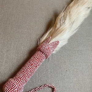 May include: A white horsehair whisk with a red and white beaded handle and a matching beaded strap.
