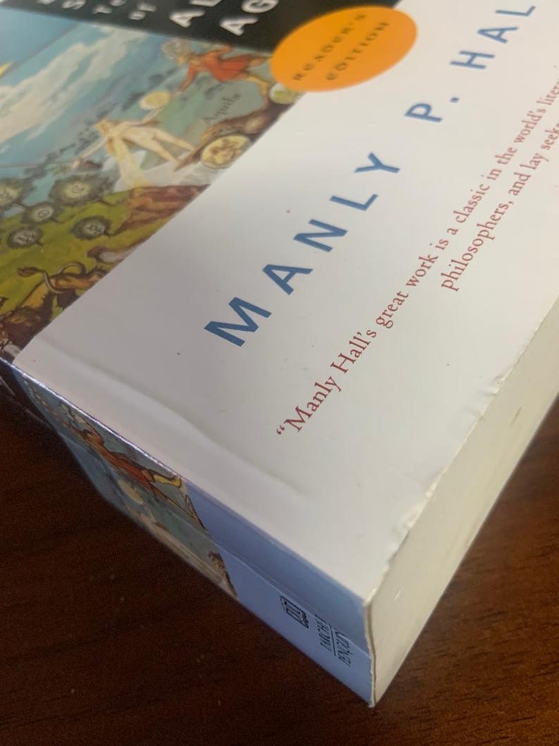 Pode incluir: Um livro branco com o t&iacute;tulo "The Story of Alchemy and the Philosopher's Stone" de Manly P. Hall. A capa do livro apresenta uma ilustra&ccedil;&atilde;o colorida de um mapa com pessoas e animais.