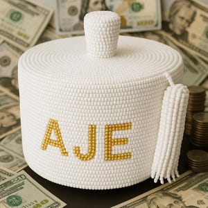 May include: White beaded piggy bank with a gold tassel and the name "AJE" spelled out in gold beads.