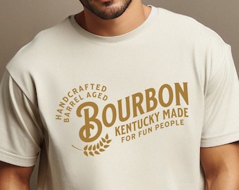 May include: A beige t-shirt with a brown graphic that says "Bourbon Kentucky Made For Fun People" and "Handcrafted Barrel Aged" in a circle around the word "Bourbon".