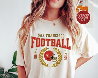 May include: A beige t-shirt with a vintage-style graphic of a football helmet and the text "SAN FRANCISCO FOOTBALL 19 46".