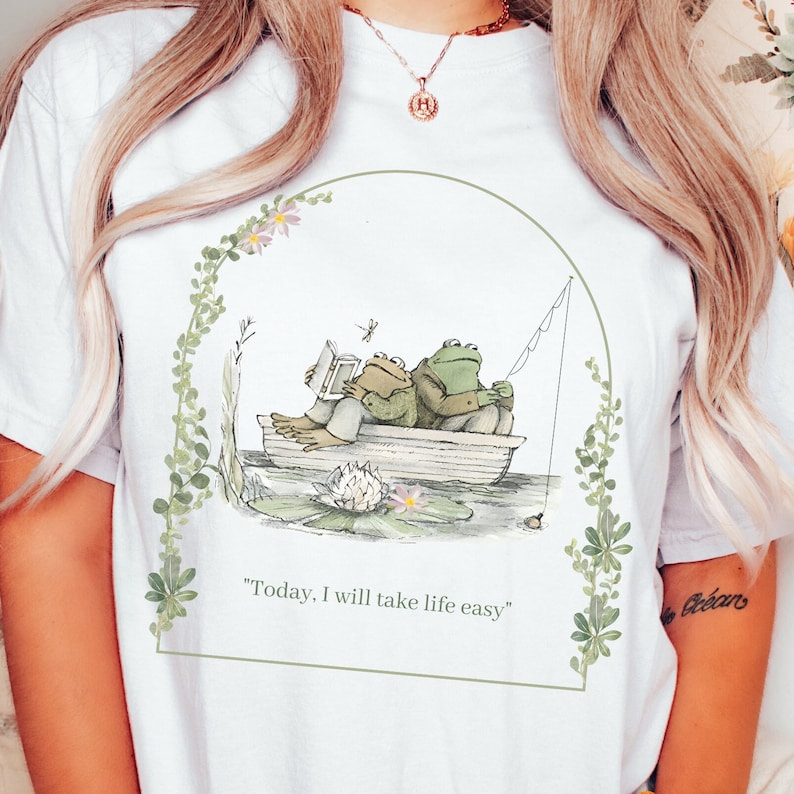 May include: White t-shirt with a green frog illustration. The frogs are in a boat on a pond with lily pads. The text "Today, I will take life easy" is printed below the illustration.