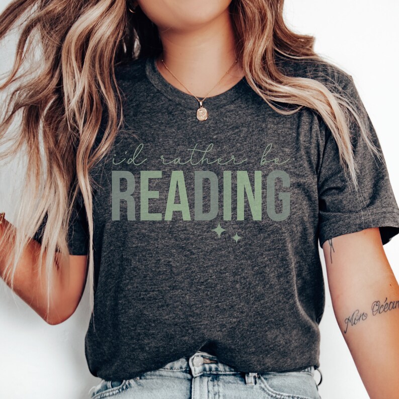 May include: A dark grey t-shirt with the text "i'd rather be READING" in green and white lettering. The shirt has a relaxed fit and a crew neck.