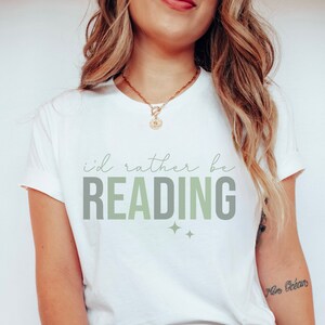 May include: White t-shirt with the text "i'd rather be READING" in green and grey lettering with two small stars below the text.