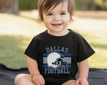 May include: A black baby onesie with a white football helmet graphic and the text "Dallas Football" in blue and white.