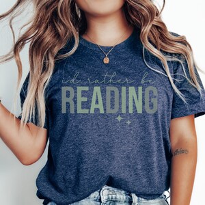 May include: A navy blue t-shirt with the text "I'd rather be reading" in green and white lettering. The shirt has a relaxed fit and is perfect for casual wear.
