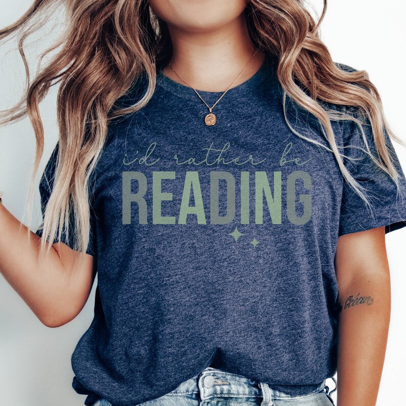 May include: A navy blue t-shirt with the text "I'd rather be reading" in green and white lettering. The shirt has a relaxed fit and is perfect for casual wear.