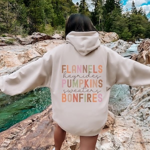 May include: A beige hoodie with the text "FLANNELS hayrides PUMPKINS sweaters BONFIRES" printed on the back in colorful letters.