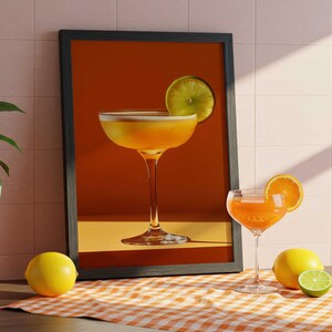 May include: A framed print of a cocktail with a lime garnish, set against a warm orange background. A cocktail glass with an orange slice and a half lime sit on a checkered cloth, with a lemon nearby.