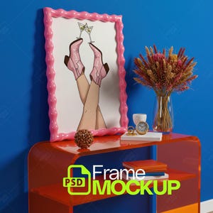 Peut inclure: Une impression d'art encadrée en rose avec une illustration de jambes portant des bottes de cowboy roses, avec des verres à martini. L'impression est sur une table rouge avec un vase de fleurs séchées, une horloge et des livres. Le texte "Frame Mockup" est visible.