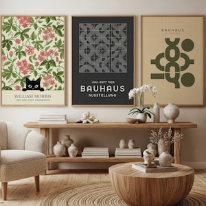Könnte beinhalten: Drei gerahmte Kunstdrucke. Der erste zeigt ein Blumenmuster mit einer schwarzen Katze und dem Text "WILLIAM MORRIS ART AND CATS EXHIBITION". Der zweite hat ein geometrisches Design mit "BAUHAUS"-Text. Der dritte zeigt abstrakte Formen.