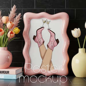 May include: A pink wavy-edged frame with a poster mockup featuring cartoon legs in pink cowboy boots holding martini glasses. A pink vase holds tulips and pampas grass. A yellow vase holds white tulips. Books with the words "GLAMOUR" and "GANUR" are stacked.