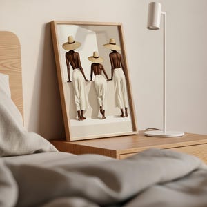 May include: Framed art print featuring three figures in white pants and straw hats, holding hands. The figures have dark skin and are set against a neutral background. The artwork is displayed on a wooden nightstand next to a white lamp.