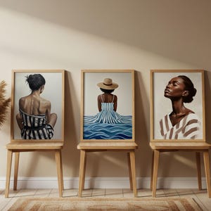 Könnte beinhalten: Drei gerahmte Kunstdrucke mit Frauen in gestreifter Kleidung. Die Kunstwerke werden auf Holzstühlen ausgestellt. Der erste Druck zeigt eine Frau in einem schwarz-weiß gestreiften Kleid. Der zweite Druck zeigt eine Frau in einem blau-weiß gestreiften Kleid und einem Strohhut. Der dritte Druck zeigt eine Frau in einem gestreiften Hemd.