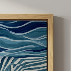 Könnte beinhalten: Ein abstraktes Gemälde in Blau- und Weißtönen, das stilisierte Wellen und ein Streifenmuster zeigt. Das Kunstwerk ist in einem Naturholzrahmen gerahmt, der der kühlen Farbpalette Wärme verleiht. Das Gemälde erinnert an das Meer.