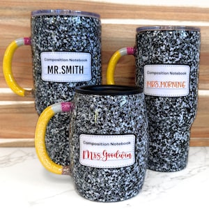 May include: Three black and white speckled travel mugs with yellow and pink pencil-shaped handles. Each mug has a white label with the text "Composition Notebook" and a teacher's name: "MR. SMITH", "MRS. MORNING", and "Mrs. Goodwin".