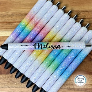 May include: A group of 12 white glitter pens with a rainbow ombre effect. The pens are personalized with the name "Melissa".