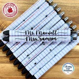 May include: A stack of personalized pens with a white and blue grid pattern and silver glitter. The pens are labeled "Mr. Maxwell" and "Mrs. Samson".
