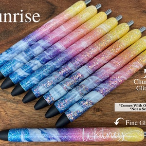 Puede incluir: Un conjunto de diez bol&iacute;grafos coloridos con un degradado de purpurina rosa, azul y amarilla. Los bol&iacute;grafos tienen un dise&ntilde;o de espiral blanco y est&aacute;n etiquetados como "Sunrise". El texto "Chunky Glitter" y "Fine Glitter" tambi&eacute;n es visible en la imagen.