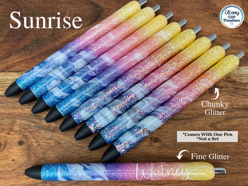 Puede incluir: Un conjunto de diez bol&iacute;grafos coloridos con un degradado de purpurina rosa, azul y amarilla. Los bol&iacute;grafos tienen un dise&ntilde;o de espiral blanco y est&aacute;n etiquetados como "Sunrise". El texto "Chunky Glitter" y "Fine Glitter" tambi&eacute;n es visible en la imagen.