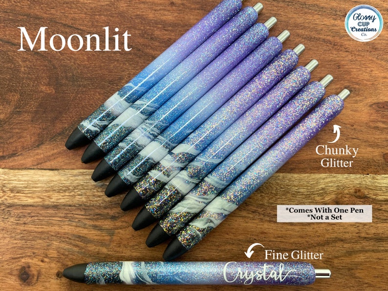 Puede incluir: Un conjunto de ocho bol&iacute;grafos con un degradado de purpurina azul y morada. Los bol&iacute;grafos tienen un dise&ntilde;o de m&aacute;rmol blanco y est&aacute;n etiquetados como "Moonlit" y "Crystal". El texto "Chunky Glitter" y "Fine Glitter" tambi&eacute;n es visible en la imagen. El texto "*Comes With One Pen *Not a Set" tambi&eacute;n es visible en la imagen.