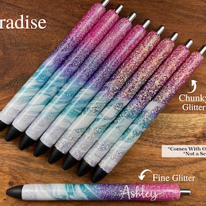 Puede incluir: Un conjunto de ocho bol&iacute;grafos con un dise&ntilde;o marmoleado y purpurina. Los bol&iacute;grafos tienen un degradado de colores rosa, morado y azul. El texto "Paradise" es visible en la parte superior de la imagen. El texto "Chunky Glitter" y "Fine Glitter" es visible en la parte inferior de la imagen. El texto "*Comes With One Pen *Not a Set" tambi&eacute;n es visible en la parte inferior de la imagen.