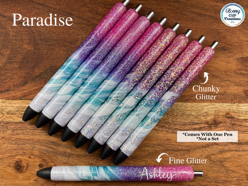 Puede incluir: Un conjunto de ocho bol&iacute;grafos con un dise&ntilde;o marmoleado y purpurina. Los bol&iacute;grafos tienen un degradado de colores rosa, morado y azul. El texto "Paradise" es visible en la parte superior de la imagen. El texto "Chunky Glitter" y "Fine Glitter" es visible en la parte inferior de la imagen. El texto "*Comes With One Pen *Not a Set" tambi&eacute;n es visible en la parte inferior de la imagen.