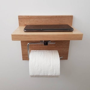 K&ouml;nnte beinhalten: Ein Holzregal mit einem Toilettenpapierhalter und einem kleinen Regal f&uuml;r ein Telefon oder andere kleine Gegenst&auml;nde. Das Regal ist an einer wei&szlig;en Wand montiert.
