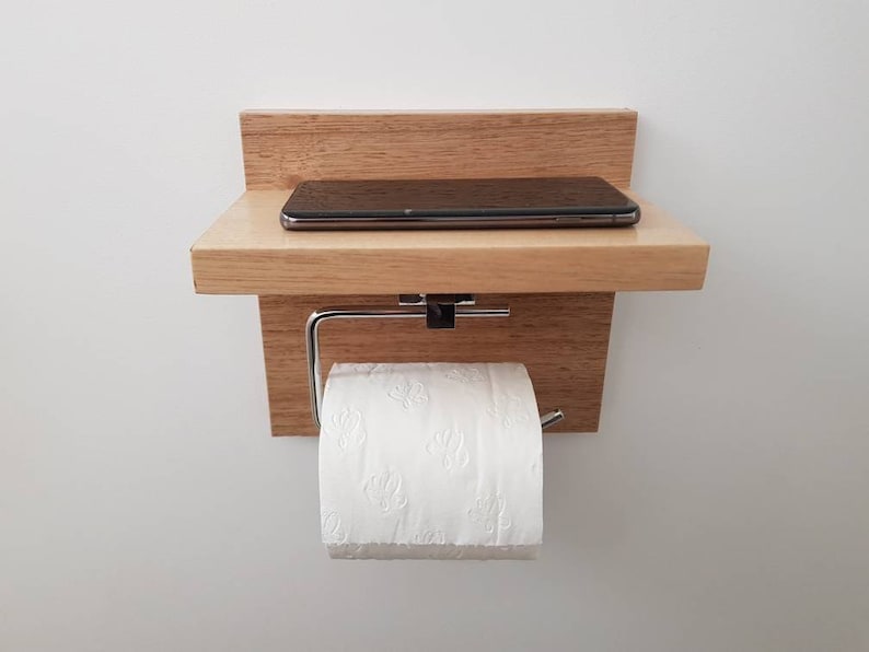K&ouml;nnte beinhalten: Ein Holzregal mit einem Toilettenpapierhalter und einem kleinen Regal f&uuml;r ein Telefon oder andere kleine Gegenst&auml;nde. Das Regal ist an einer wei&szlig;en Wand montiert.