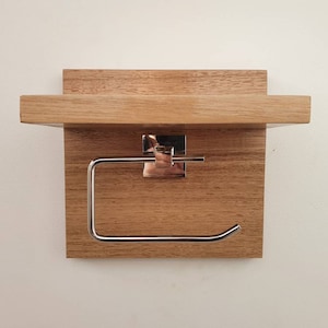 K&ouml;nnte beinhalten: Ein Toilettenpapierhalter aus Holz mit einem Regal. Der Halter ist aus hellbraunem Holz und hat einen Toilettenpapierrollenhalter aus Chrom.