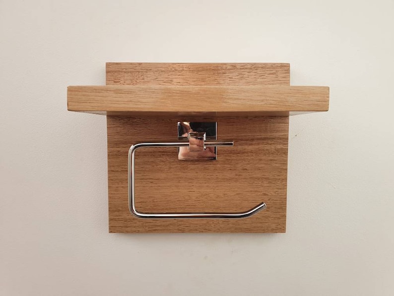 K&ouml;nnte beinhalten: Ein Toilettenpapierhalter aus Holz mit einem Regal. Der Halter ist aus hellbraunem Holz und hat einen Toilettenpapierrollenhalter aus Chrom.
