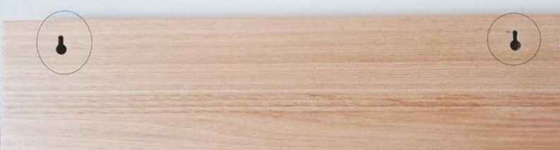 K&ouml;nnte beinhalten: Nahaufnahme einer hellbraunen Holzplatte mit zwei vorgebohrten L&ouml;chern zum Aufh&auml;ngen.